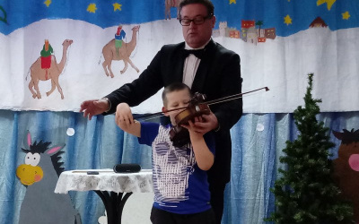chłopiec z pomocą Pana Jacka stojącego za nim, gra na skrzypcach