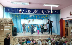 Pan Jacek wraz z dziećmi tańczy walca na scenie, stoją w rzędzie, dziećmi poruszają się rytmicznie do przodu i do tyłu