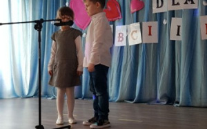 chłopiec w białej koszuli i jeansach oraz dziewczynka w beżowej sukience śpiewają przy mikrofonie