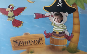 chłopiec pozuje do zdjęciawsuwającgłowę w otwór planszy - pirat spoglądający przez lunetę na napis Nibylandia