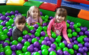 trzy zadowolone dziewczynki w baseniku z zielono-fioletowymi piłeczkami