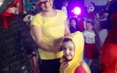 Pani Ania w kolorowycm kapeluszu i żółtej koszulce poprawia dziewczynce zsunięty strój żółciutkiego kurczaczka