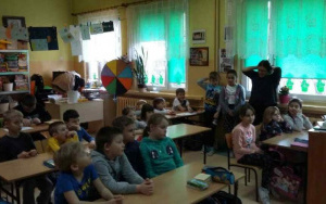 przedszkolaki w ławkach wraz ze starszymi kolegami obserwują panią nauczycielkę