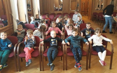 przedszkolaki siedzą wygodnie na bordowych fotelach i oczekują na koncert.