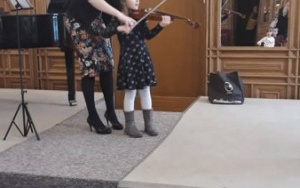 Dziewczynka z pomocą skrzypaczki gra na skrzypcach