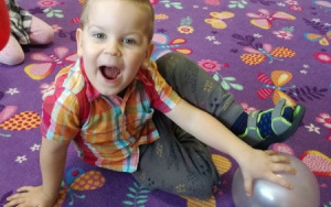Uśmiechnięty chłopiec przyciska srebrny, napompowany balonik do dywanu