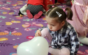 dziewczynka w sukience w czarno - białą kratkę dmucha w napompowany biały balonik