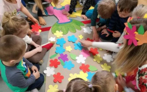 Dzieci na dywanie przyklejają do sukni Pani Wiosny papierowe kwiaty