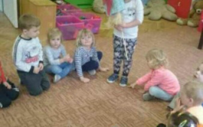 dzieci w kole na dywanie, przy kole stoi dziewczynka trzymająca kukłę Marzanny