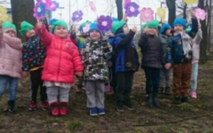 uśmiechnięte dzieci z papierowymi kwiatami w dłoniach stoją na górce