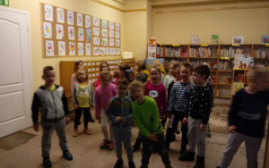dzieci śpiewaja piosenkę, z tyłu regały z książkami