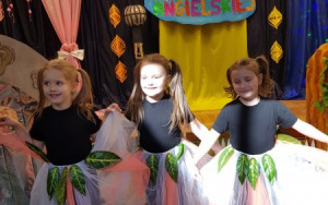 trzy dziewczynki na scenie, trzymają rozłożone spódniczki, stoją pod napisem V Festiwal Piosenki Angielskiej
