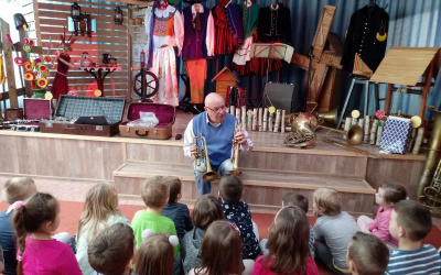 mężczyzna prezentuje zainteresowanym dzieciom instrumenty dęte blaszane - trąbki