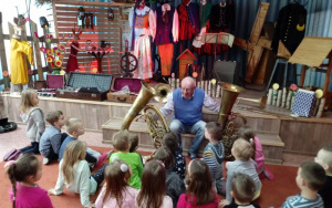 mężczyzna prezentuje zainteresowanym dzieciom instrumenty dęte blaszane 