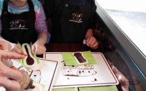 chłopiec i dziewczynka w czapkach i fartuchach kucharskich spoglądają na foremki wypełnione ciepłą czekoladą