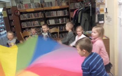 dzieci bawią się chustą animacyjną,w tle regały z książkami