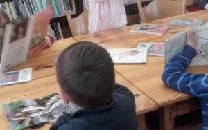 dzieci przy dużym stoleoglądają kolorowe książki,dziewczynka w różowej bluzie pokazuje książkę, którą wybrała