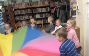 dzieci bawią się chustą animacyjną,w tle regały z książkami