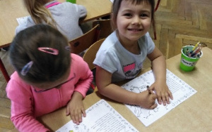 dwie uśmiechnięte dziewczynki przy stoliku kolorują obrazek
