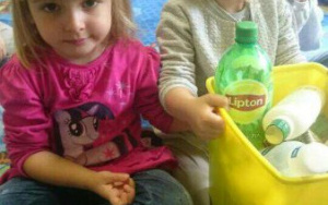 dwie dziewczynki trzymają żółty pojemnik z plastikowymi odpadami