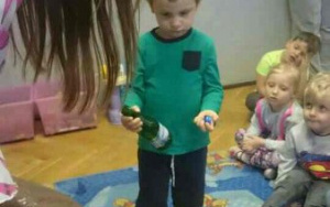chłopiec w zielonej bluzce trzyma w rączkach zieloną butelkę i korek, zastanawia się, do którego kosza wrzucićśmieci
