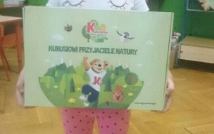 dziewczynka trzyma tekturowe pudełko na nim napis Kubusiowi przyjaciele natury