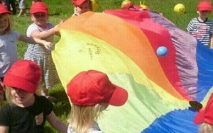 dzieci podrzucająna kolorowej chuście animacyjnej plastikowe piłki