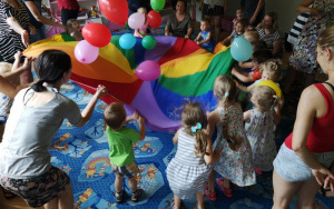 zaangażowane, radosne dzieci, wraz z rodzicami, podrzucają na chuście animacyjnej, do góry, kolorowe balony