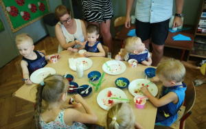 dzieci w niebieskich fartuszkach zajadają lody przy stolikach