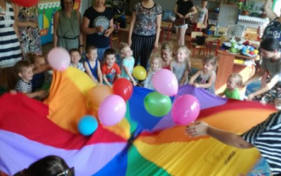 dzieci i rodzice bawią się z chustąanimacyjną, na chuście kolorowe balony