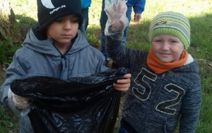 dwaj chłopcy z czarnym workiem na śmieci i foliową rękawiczką na rączce