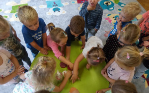 dzieci nachylone nad zielonym stolikiem oglądają, dotykają i wąchają różne mydełka