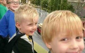 uśmiehnięci chłopcy oglądają makietę - kolejka wyjeżdżaąca z tunelu, czerwony tramwaj na szynach