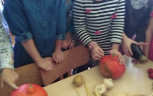 grupa dzieci wsparta o stół i krzesło przygląda się umieszczonym na stole warzywom