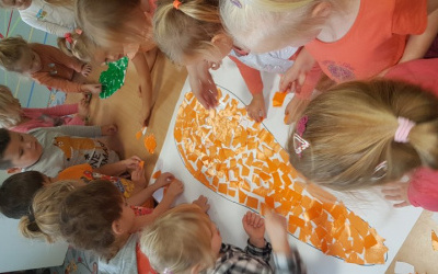 dzieci przy stole kończą wyklejać kontur marchewki pomarańczowym papierem oraz nać - zielonym
