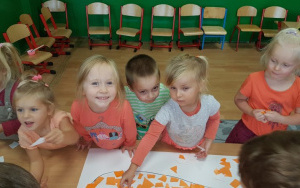 uśmiechnięte dzieci pry stoliku podczas wyklejania konturu marchewki