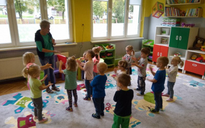 dzieci stoją na dywanie, wraz z nauczycielką śpiewają piosenkę, naśladują rączkami czynność krojenia surówki