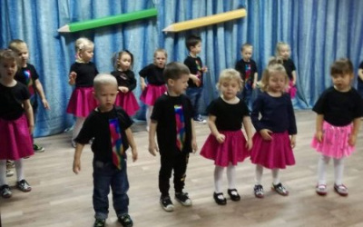dzieci w czarnych tshirtach, chłopcy w tęczowych krawatach, dziewczynki w różowych spódniczkach, stoją w rozsypce na scenie i śpiewają piosenkę