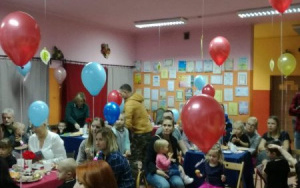 Rodzice i dzieci goszczą się przy pysznie zastawionych stołach, pomiędzy gośćmi unoszą się kolorowe balony