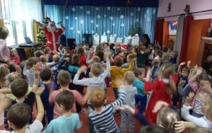 Mikoła z mikrofonem wymachuje ramionami nad głową, dzieci naśladują ruchy Mikołaja