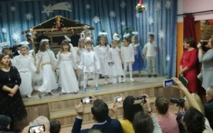 na scenie dzieci z grupy 6, latkow w strojach aniołków śpiewają, w tle szopka ze świetą Rodziną, po lewej i prawe stronie nauczycielki, na wydowni rodzice