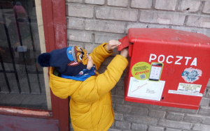 chłopiec w żółtej kurtce i granatowej czapce wrzuca kartkę do czerwonej skrzynki pocztowej