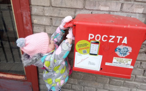 dziewczynka w różowe czapce z pomponem wrzuca kartkę do czerwonej skrzynki pocztowej