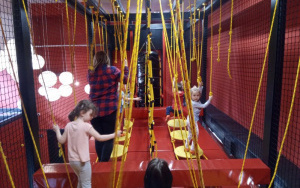 dzieci przechodzą po ruchomych przeszkodach podwieszonych pod sufitem na żółtych linach