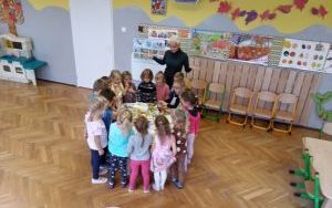  dzieci wraz  z nauczycielką  stoją dookoła stolika z kolorowymi bajkami