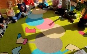 dzieci w półokręgu na dywanie, przed nimi kolorwe tablice demonstracyjne