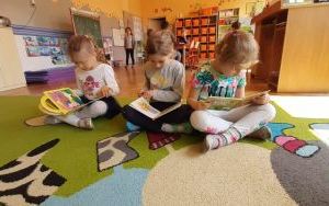 trzy dzieczynki na dywanie z zainteresowniem oglądają książeczki