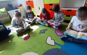 dzieci na dywanie z zainteresowniem oglądają książeczki