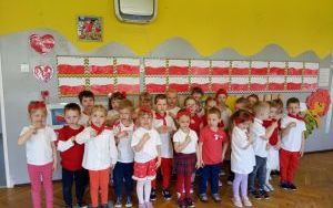 Dzieci w białoczerwonych strojach śpiewają piosenkę, w tle polskie flagi wykonane przez dzieci