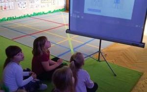 Dzieci na dywanie skupione na prezentacji multimedialnej